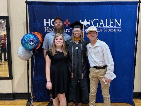 Kacie Antrobus wearing a graduation cap and gown stands with family members in front of an HCA Healthcare and Galen College of Nursing backdrop.
