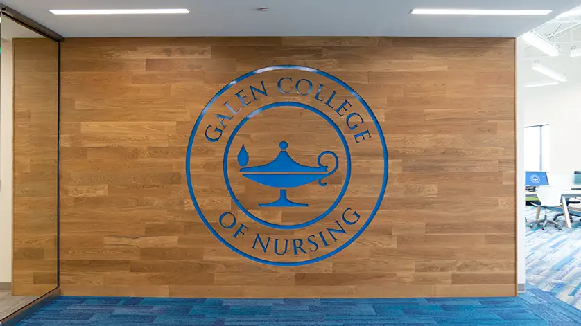 Wood wall with Galen College of Nursing logo on it.