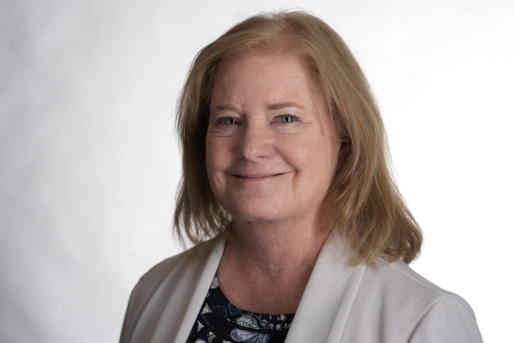 Professional portrait of a woman wearing a light-colored blazer over a patterned top, photographed against a neutral studio background.