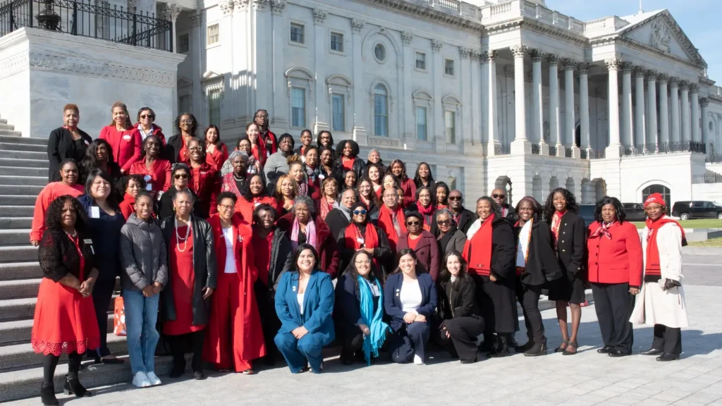 A large, diverse group of approximately 50 people, primarily Black women, posing for a group photo on the steps of the U.S. Capitol building in Washington, D.C.