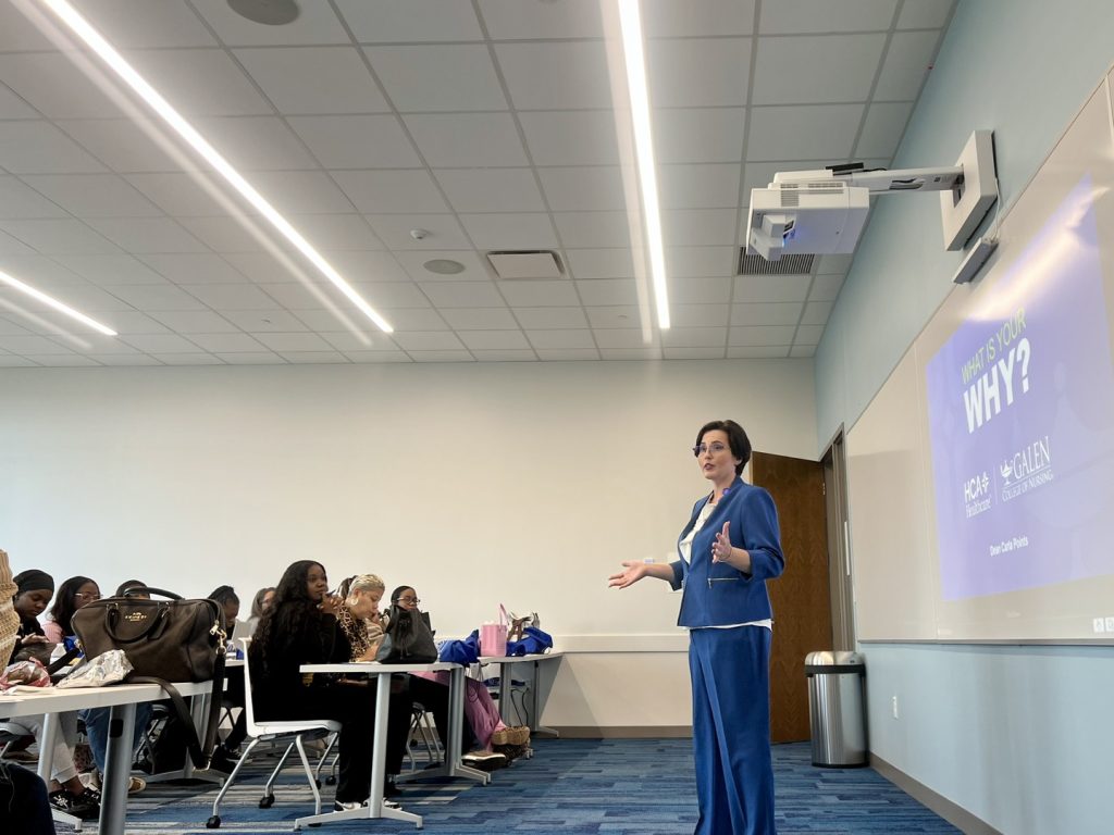 Presenter speaking to nursing students in a classroom, with a projected slide behind them during an educational session.