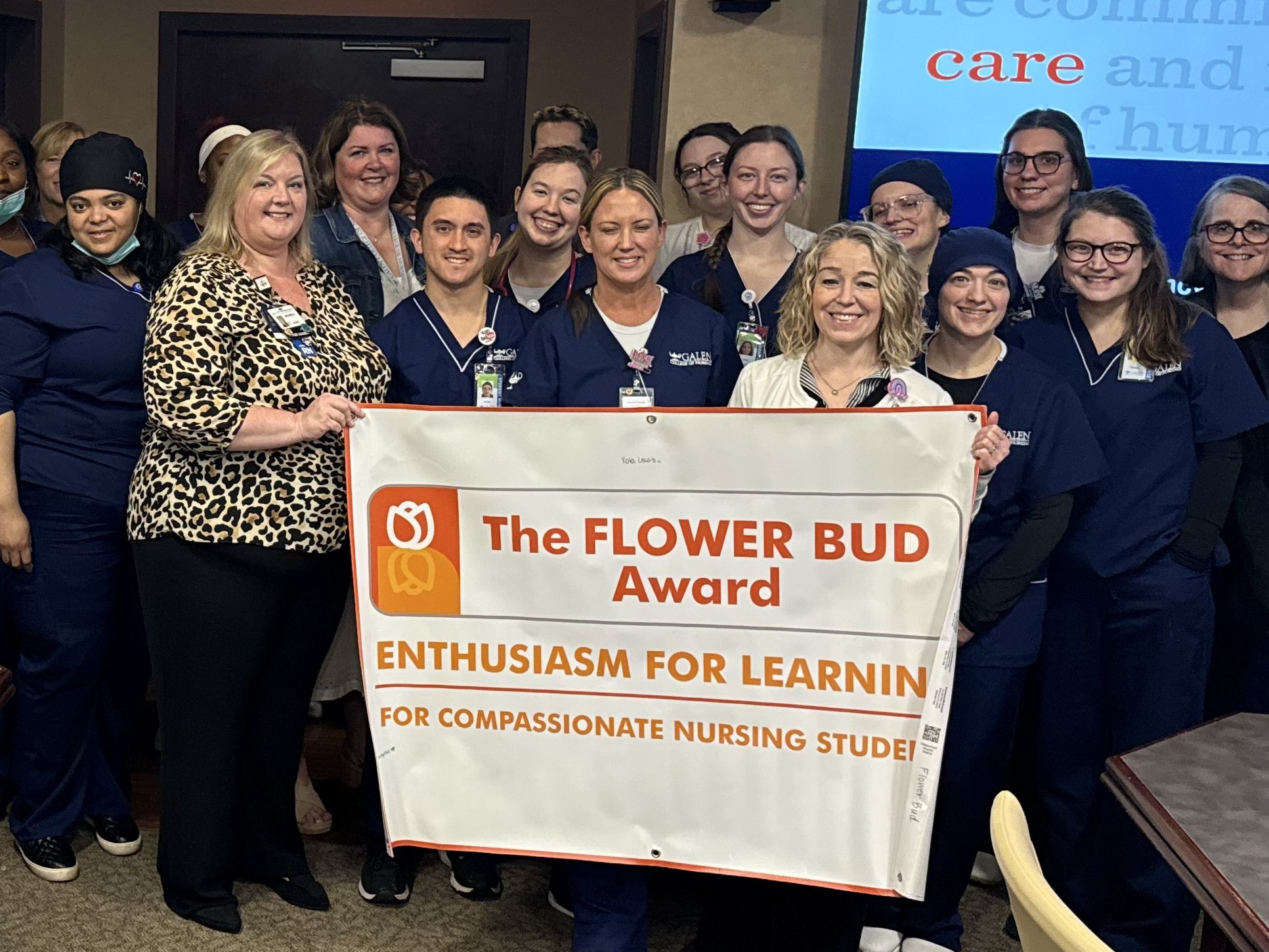 A large group of nursing students and staff stand in a conference room holding a “Flower Bud Award” banner.