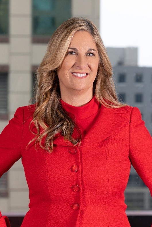 Faculty member wearing a red jacket, standing outdoors with a city building in the background.