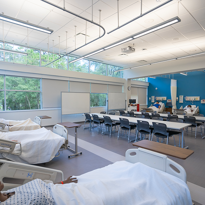 the Gainesville simulation lab, showing beds with mannequins, classroom tables and chairs