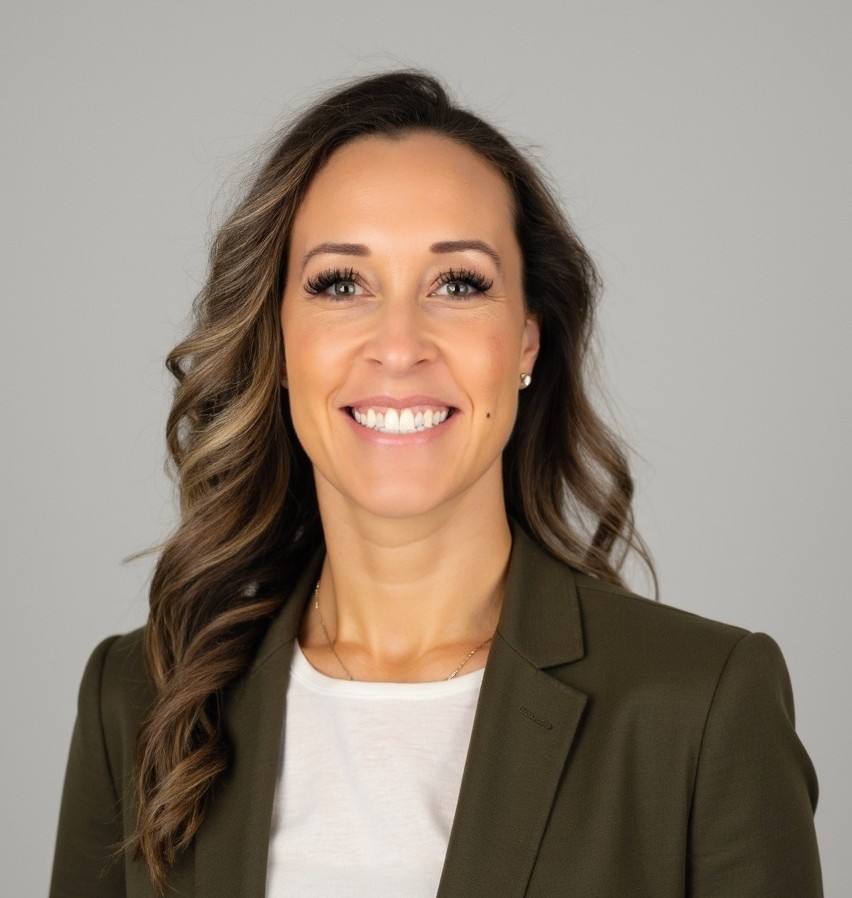 Nichole Urban wearing a green blazer and white top, standing against a neutral background for a professional portrait.
