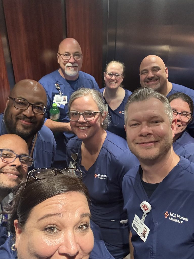Group of nurses wearing scrubs gathered closely together inside a hospital elevator.