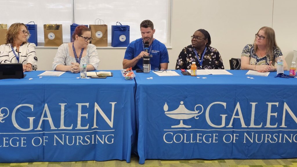 Image of five panelists sitting behind two long tables with blue tablecloths that have the Galen College of Nursing logo lockup. 