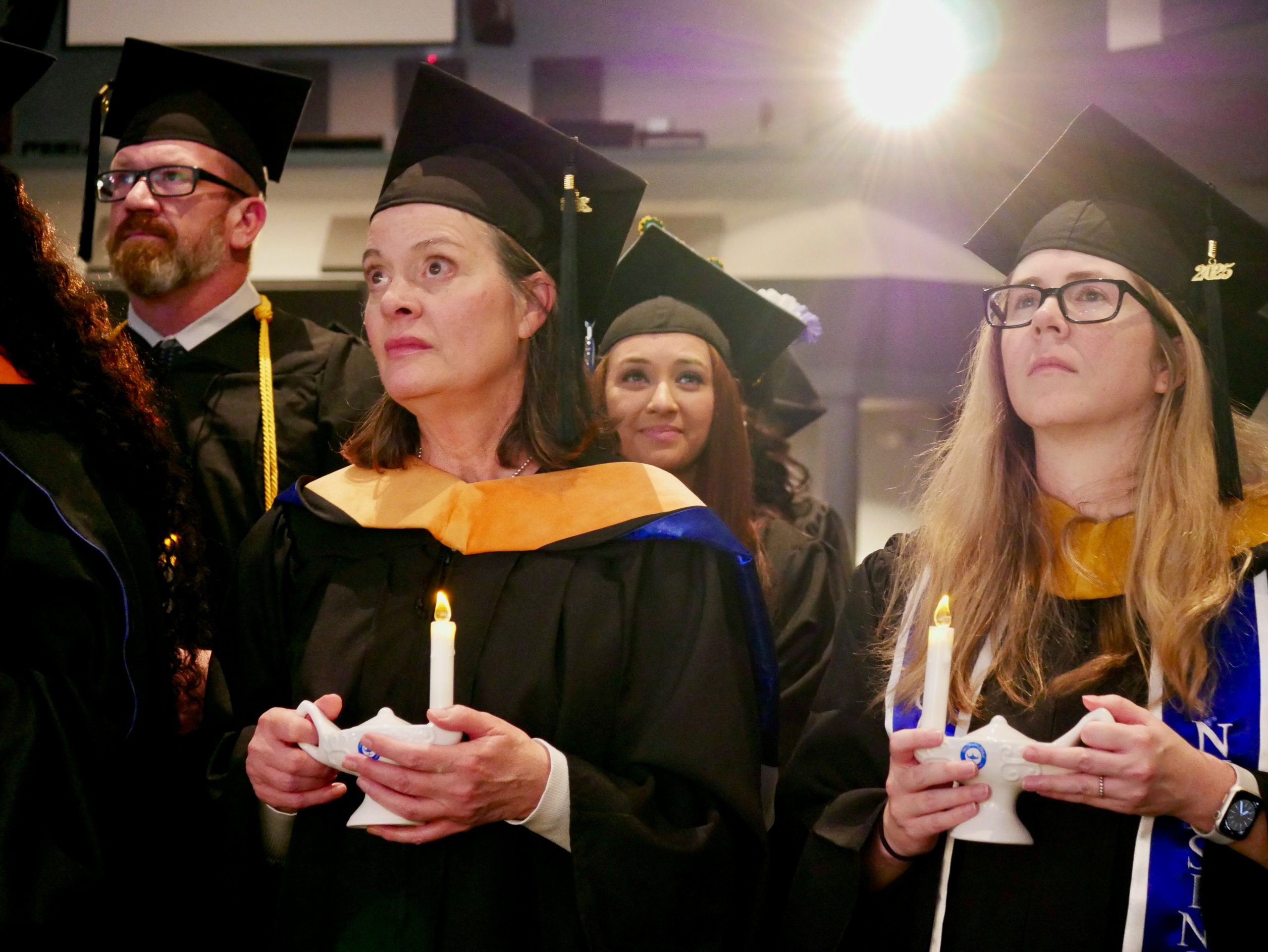 Graduates in caps and gowns holding lit candles during a commencement ceremony.