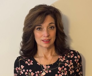 A woman sits for a professional headshot against a white wall. 