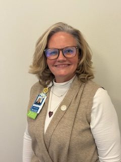 A smiling woman takes a photo in front of a white wall. 