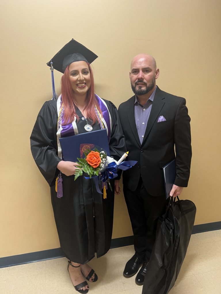 Melissa Alvarez in graduation cap and gown holding her diploma and flowers, standing beside Dr. Yunieski Farradas in professional attire.