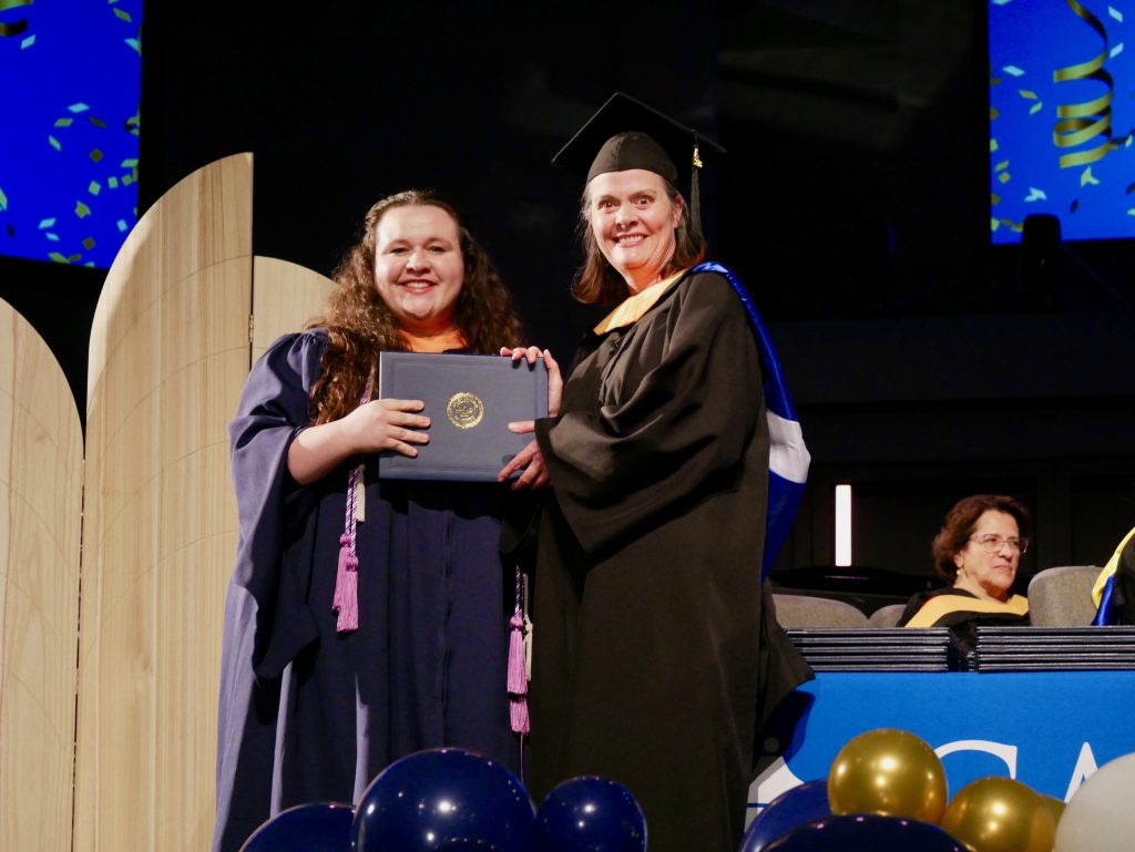 Graduate in cap and gown receiving a diploma on stage.