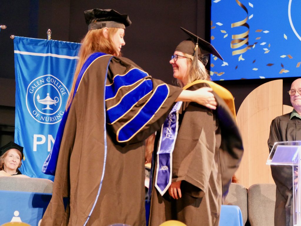 Faculty member placing a graduation hood on a graduate during the ceremony.