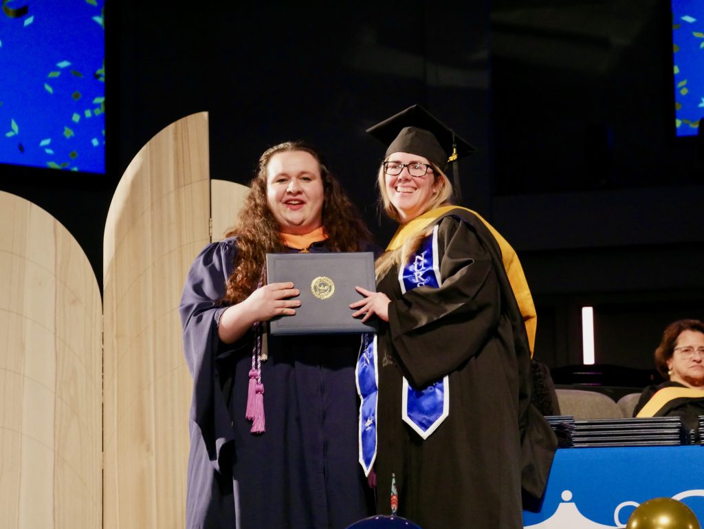 Graduate in cap and gown receiving a diploma on stage.