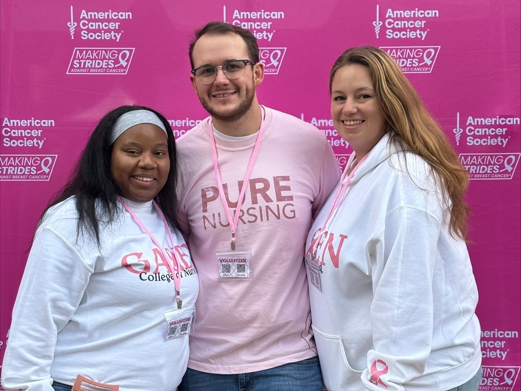 Three individuals standing in front of a pink backdrop with American Cancer Society and Making Strides Against Breast Cancer logos.