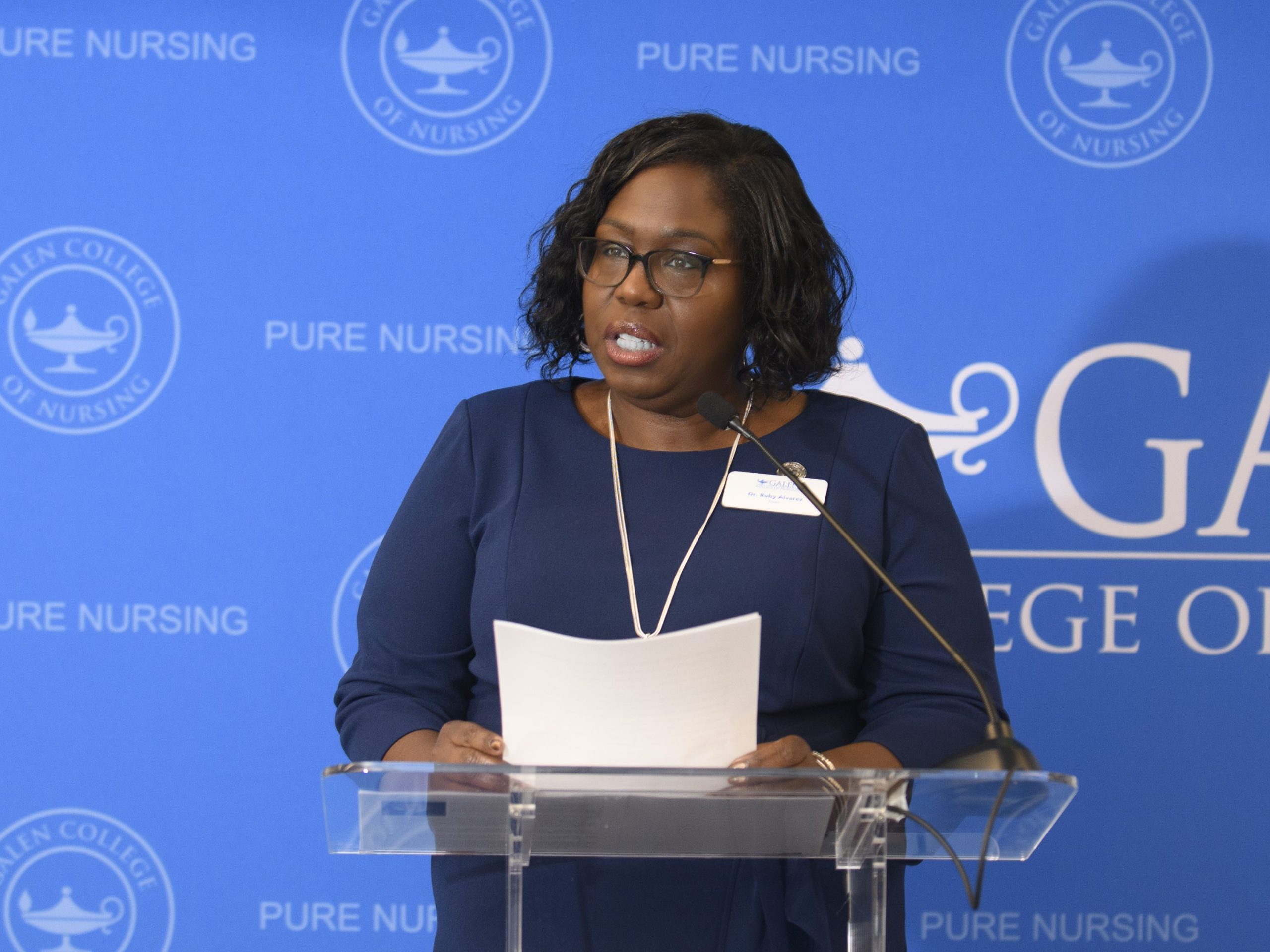 A speaker stands at a clear podium during a Galen College of Nursing grand opening event.