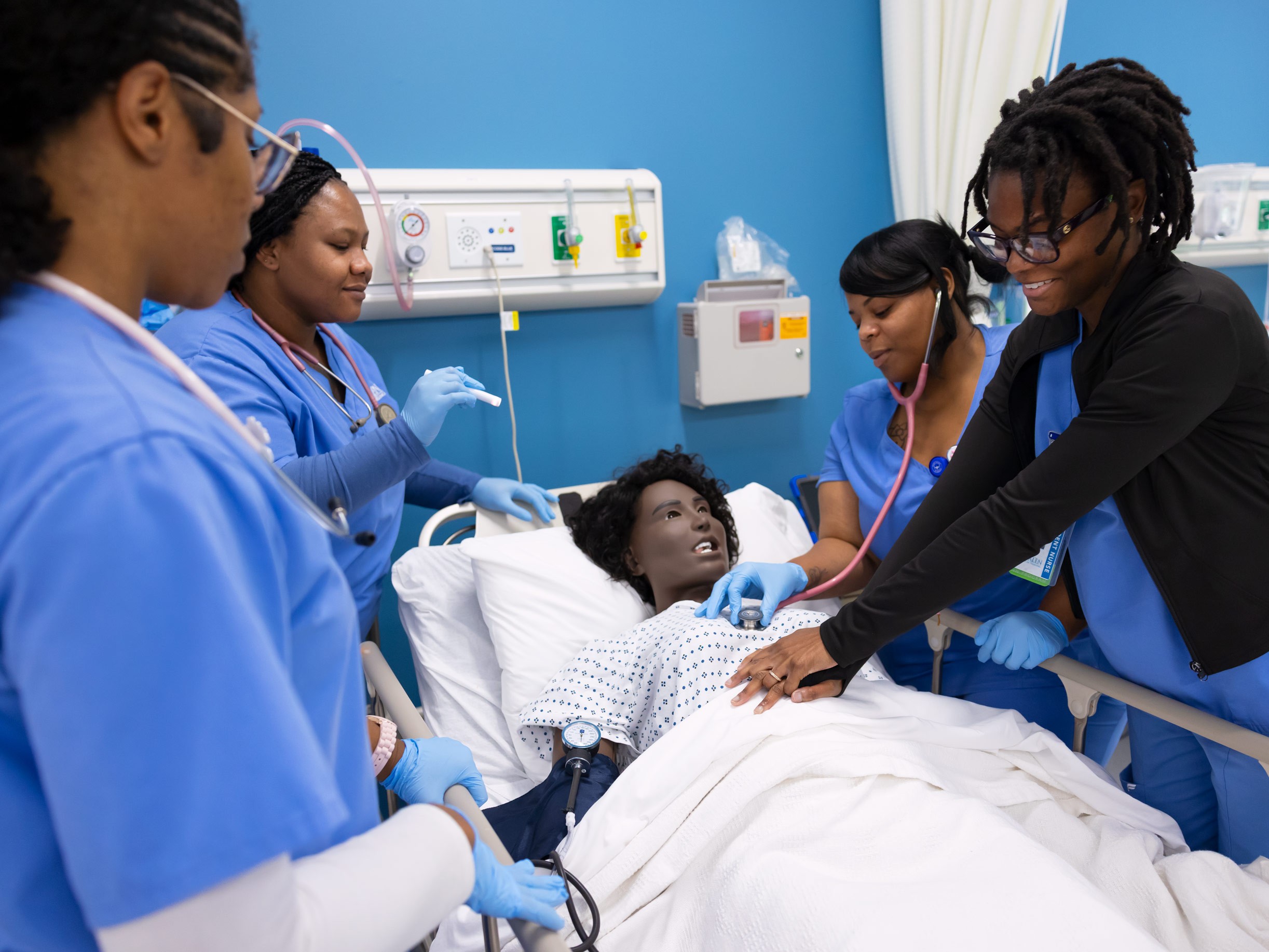 Nursing students practice patient care in a simulation lab, monitoring a patient in a hospital bed.