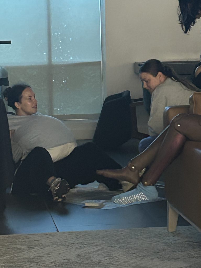 A student assists a patient mannequin positioned on a couch during a simulation, while another mannequin with visible injuries lies nearby on the floor as part of a disaster scenario.
