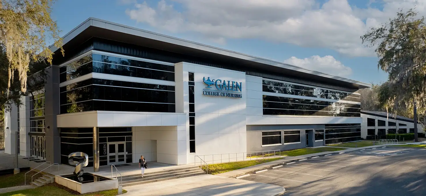 A modern Galen College of Nursing building campus in Gainesville, FL with a sleek design featuring large glass windows and white and gray paneling, surrounded by landscaping and a paved entrance.