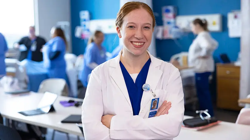 woman nursing instructor smiling at camera with simulation lab activities happening in background